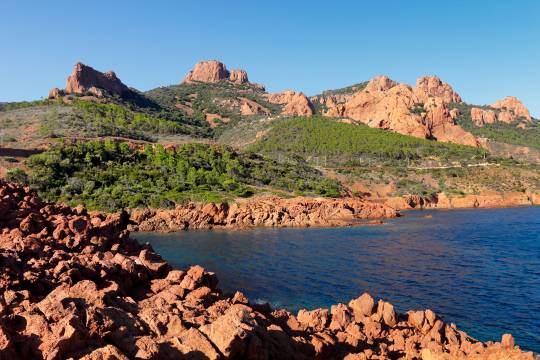 Paysage sauvage de l'Estérel avec ses roches rouges, sa végétation verdoyante et la mer Méditerranée, un arrêt incontournable lors d’un road trip en van sur la Côte d’Azur.