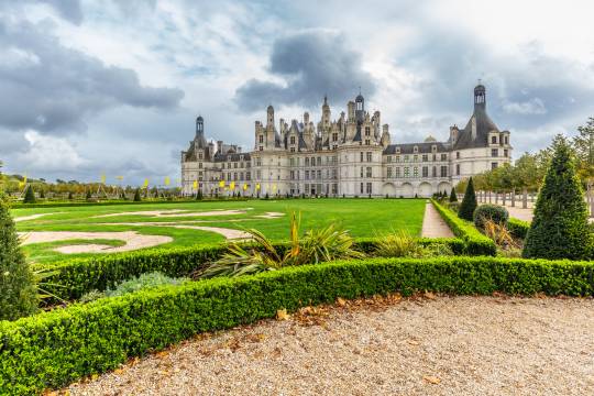 Vue majestueuse du château de Chambord et de ses jardins à la française sous un ciel nuageux, une étape culturelle incontournable lors d’un road trip en van dans la vallée de la Loire.