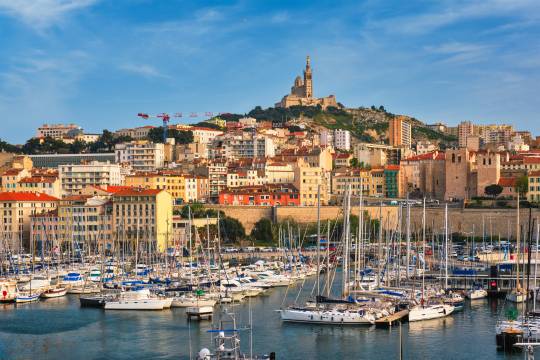 Vue pittoresque du Vieux-Port de Marseille avec ses bateaux de plaisance, les immeubles colorés et la basilique Notre-Dame de la Garde surplombant la ville, destination idéale pour un road trip en van en France.