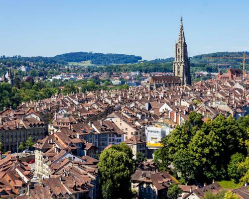 Vue panoramique de la vieille ville de Berne, capitale de la Suisse, avec ses bâtiments historiques aux toits rouges bordant la rivière Aar sinueuse, entourée par les collines verdoyantes des Préalpes bernoises