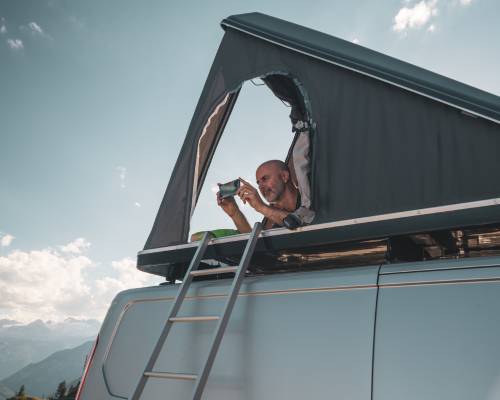 Homme profitant de la vue depuis une tente de toit sur un van aménagé en pleine nature